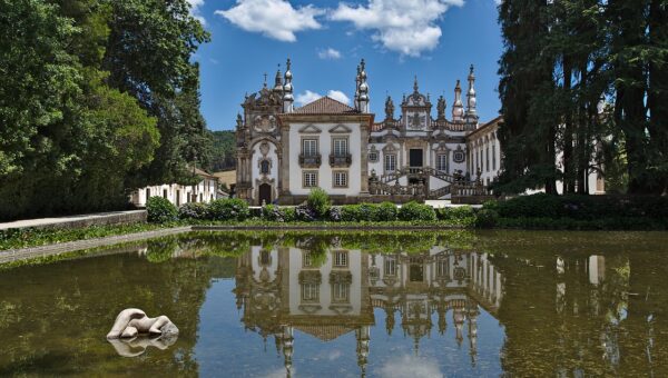 Baroque-style palace with intricate architecture reflected in a calm garden pond under a clear blue sky.