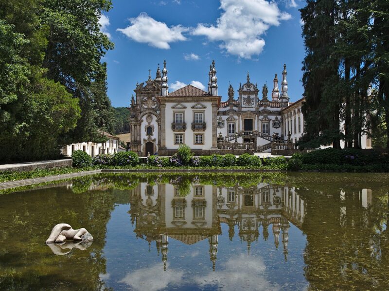 Baroque-style palace with intricate architecture reflected in a calm garden pond under a clear blue sky.