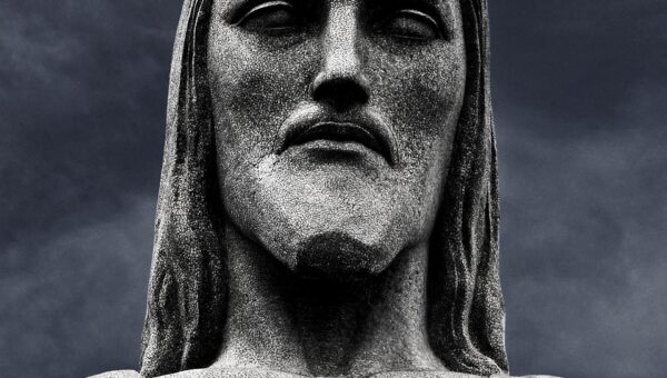 Close-up of Christ the Redeemer statue against dark clouds, symbolizing the death of Jesus Hymninges